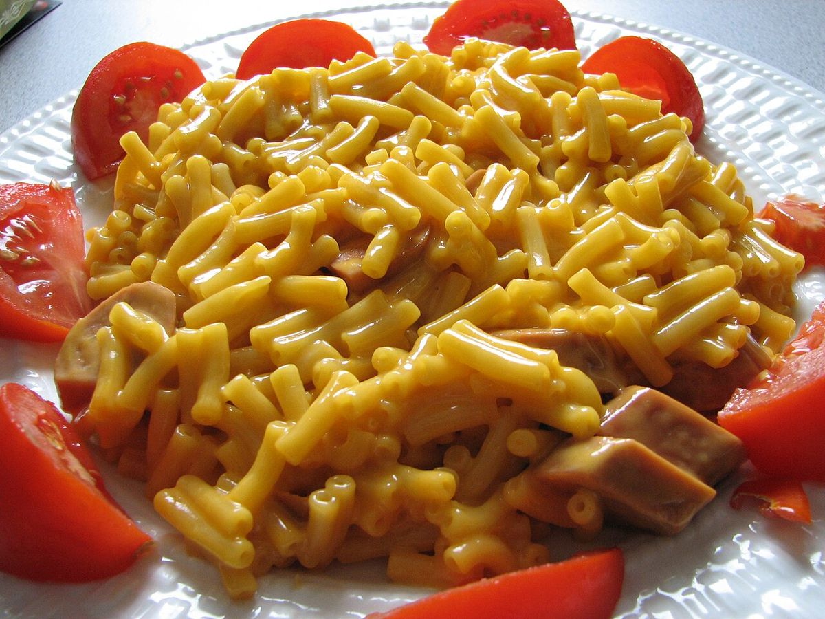Kraft Dinner (macaroni and cheese) with added cheddar and sliced vegetarian hot dogs arranged on a plate and bordered by tomato wedges. Phot