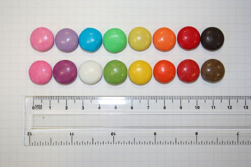 Photograph of Nestlé Smarties as sold in the UK, before (top) and after (bottom) change to natural colours. Background is 5mm squares.