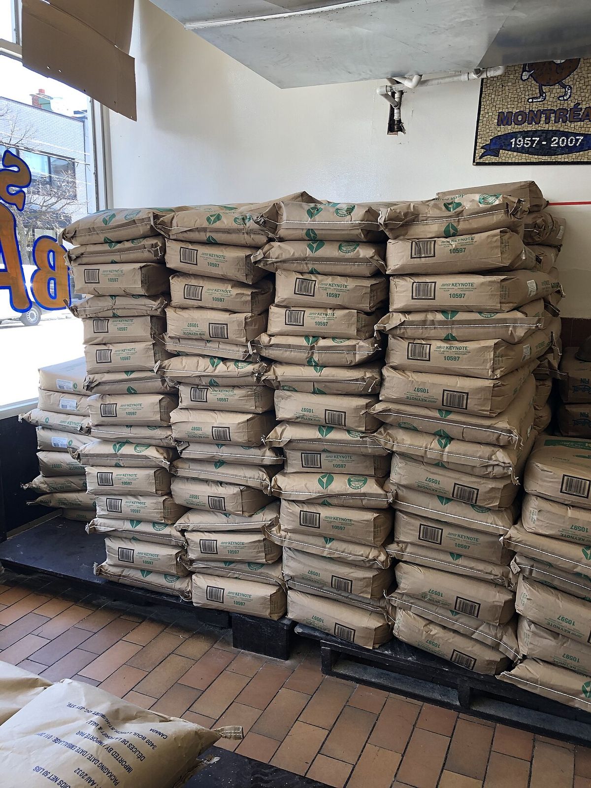 In the front of the bakery, by the window, piles of flour bags are displayed.