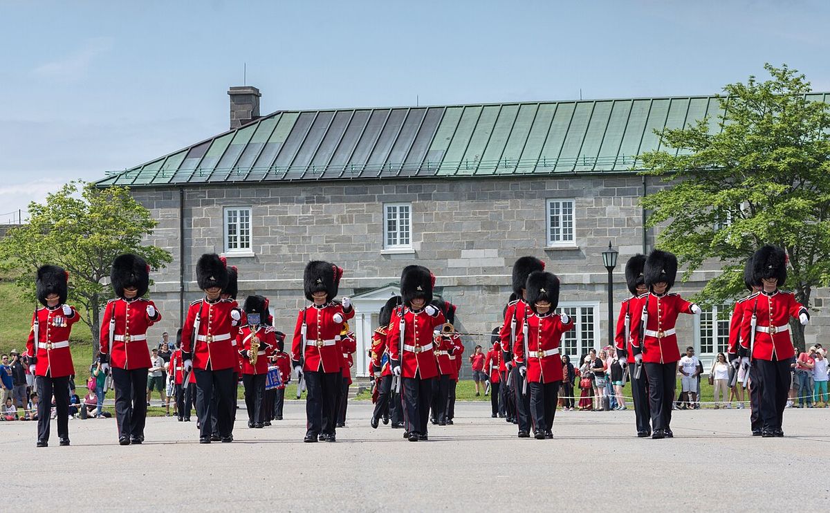 Soldiers of the Royal 22e Régiment marching past one of the stone barrack blocks of the Citadelle, its long green metal roof behind them and